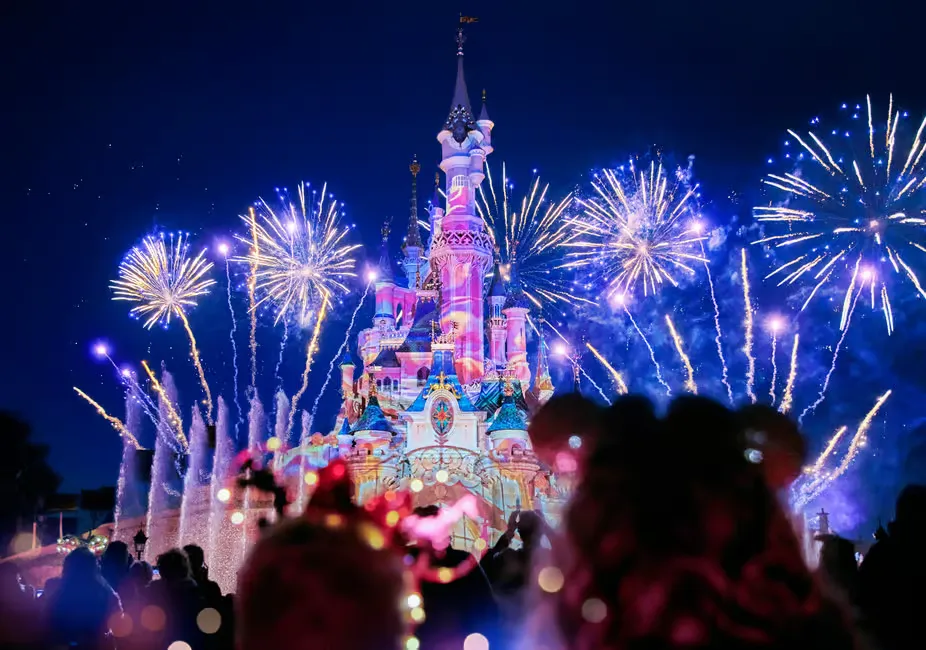Illuminated castle with vivid fireworks lighting up the night sky, colorful bursts reflect on the building, creating a magical scene.
