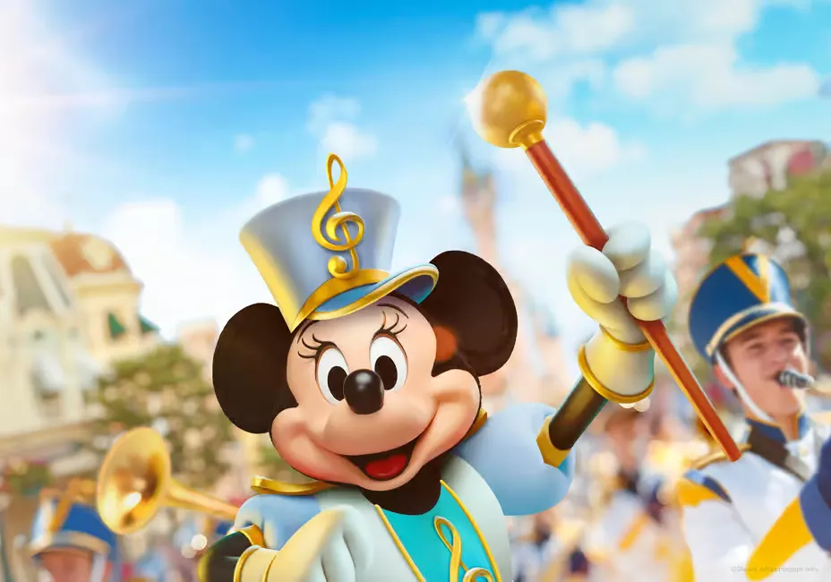 Minnie Mouse in marching band outfit, holding a baton, smiles amid a parade. Musicians in blue and yellow uniforms in the background. Bright, sunny day.